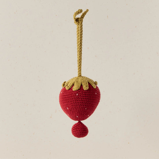 Crocheted strawberry ornament with a yellow stem on a beige background
