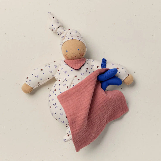Stuffed doll with a pink blanket and blue toy on a beige background
