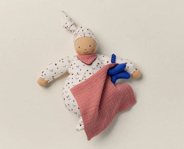Stuffed doll with a pink blanket and blue toy on a beige background