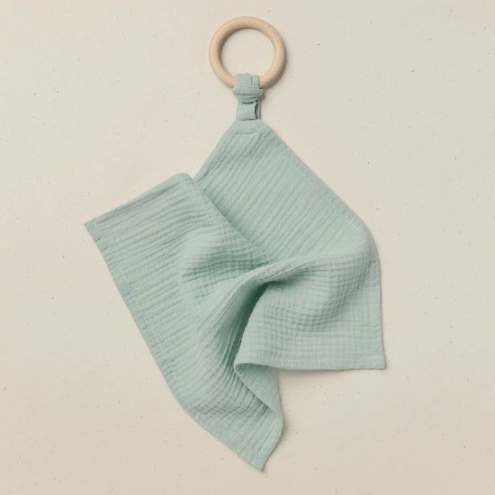Teal baby blanket with wooden ring on a beige background