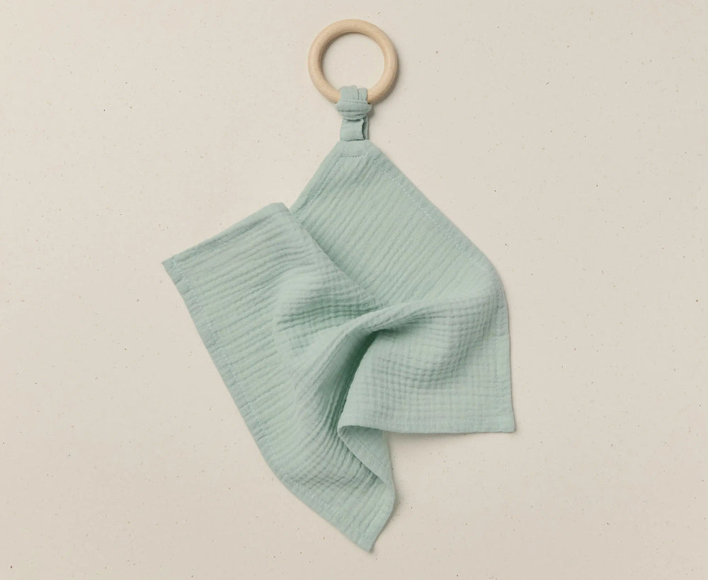 Teal baby blanket with wooden ring on a beige background