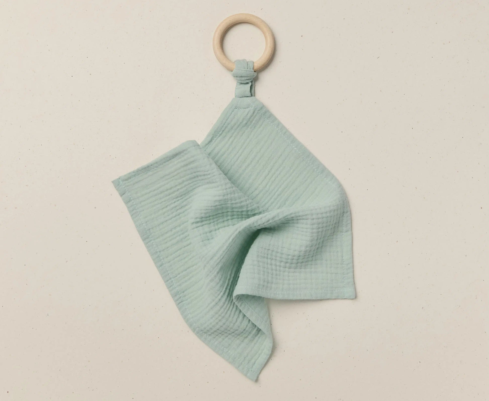 Teal baby blanket with wooden ring on a beige background