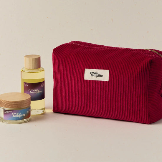 Red toiletry bag with 'amour et temple' branding next to a bottle and jar on a beige background