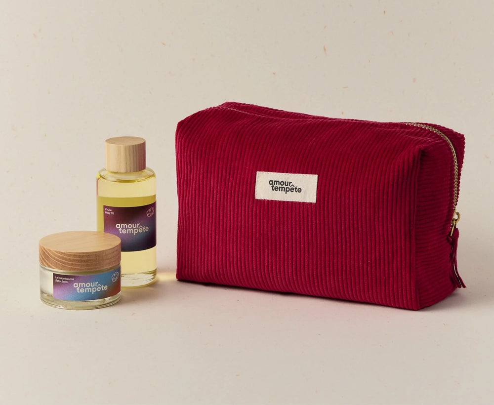 Red toiletry bag with 'amour et temple' branding next to a bottle and jar on a beige background