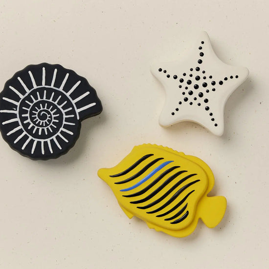 Three bath toys with geometric patterns on a beige background