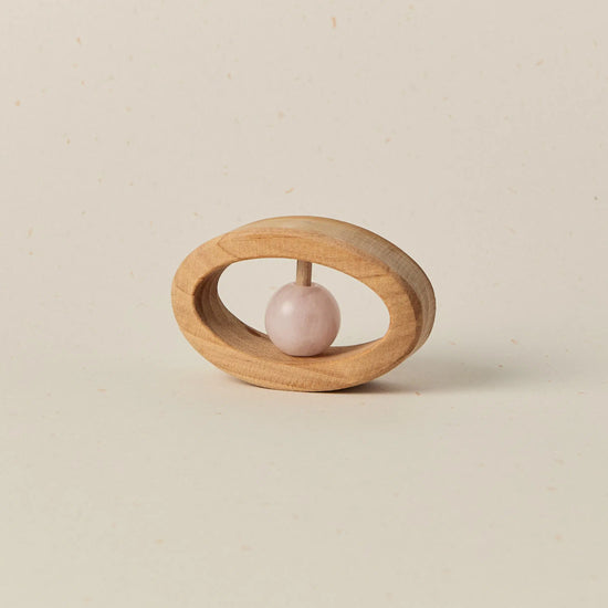 Wooden baby teether with a pink stone on a beige background