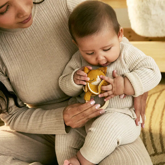 Woman holding a baby who is playing with a yellow toy on a wooden floor.