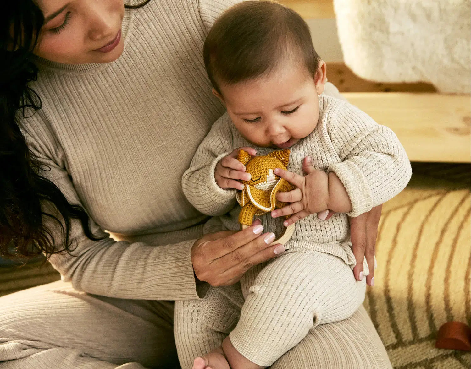 Woman holding a baby who is playing with a yellow toy on a wooden floor.