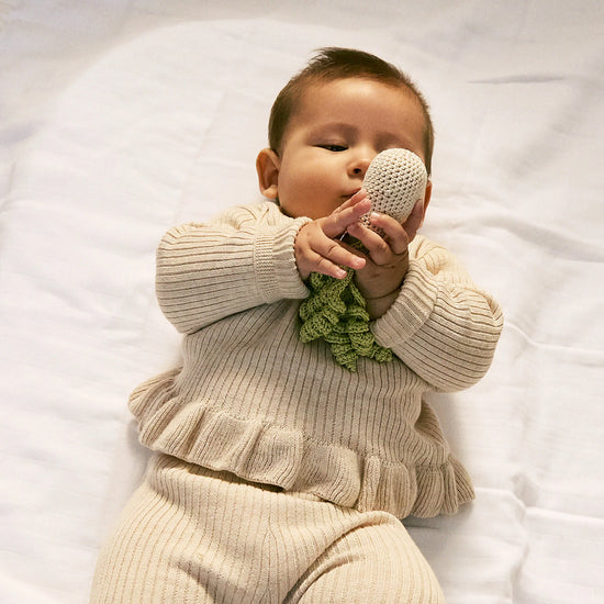 Baby in a beige outfit holding a knitted toy on a white blanket