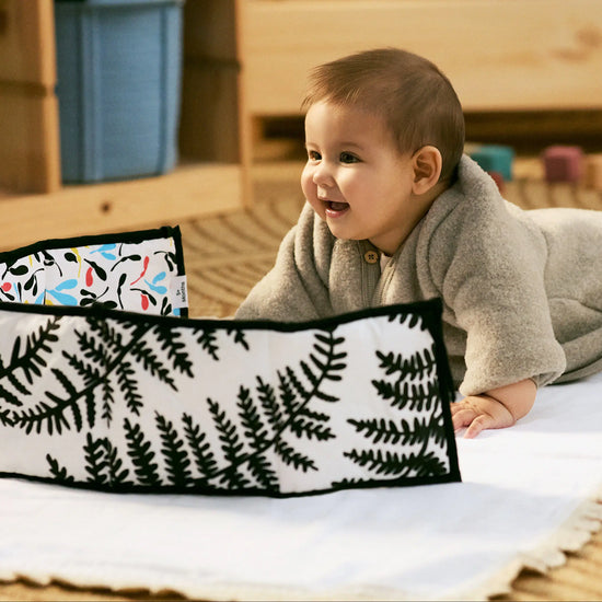 Baby lying on a wooden floor next to a floral-patterned bag