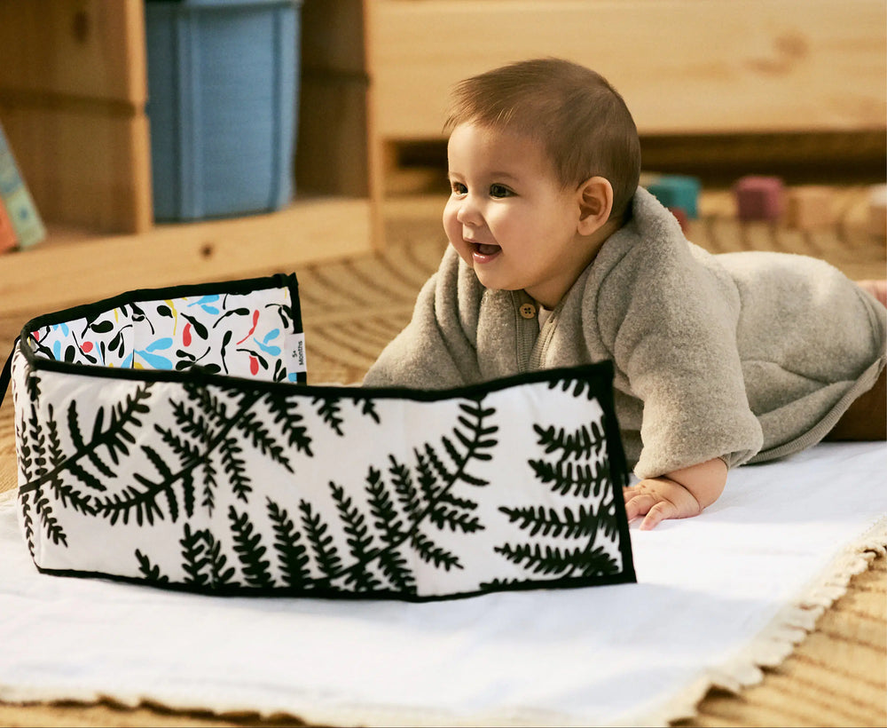 Baby lying on a wooden floor next to a floral-patterned bag