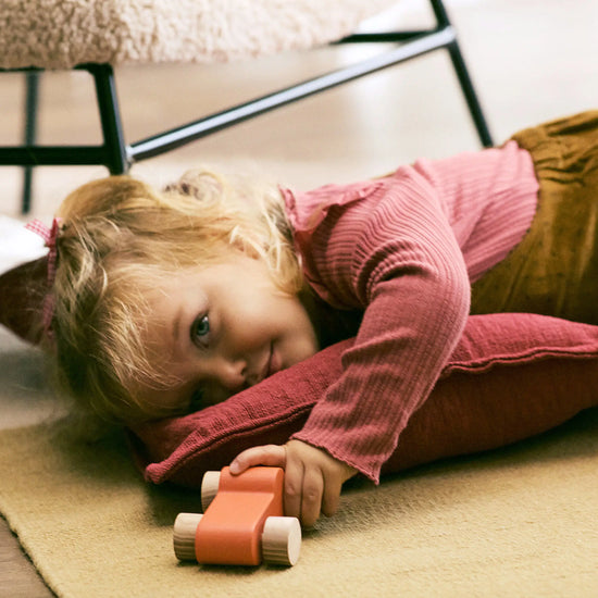 Child lying on a rug with a toy car, indoors.