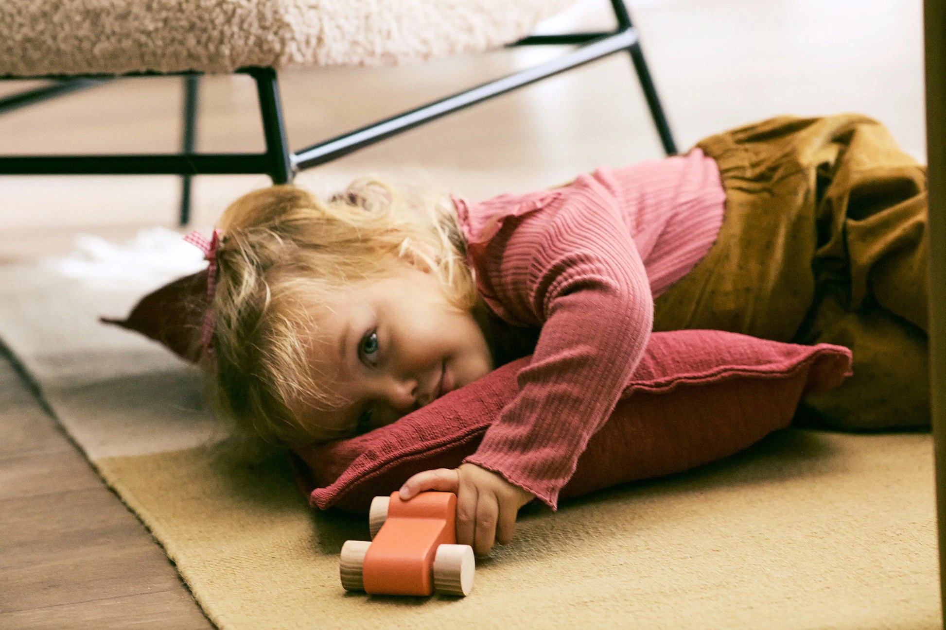 Child lying on a rug with a toy car, indoors.