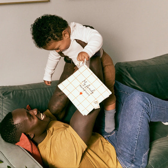Man and child sitting on a couch with a child holding a white bag.