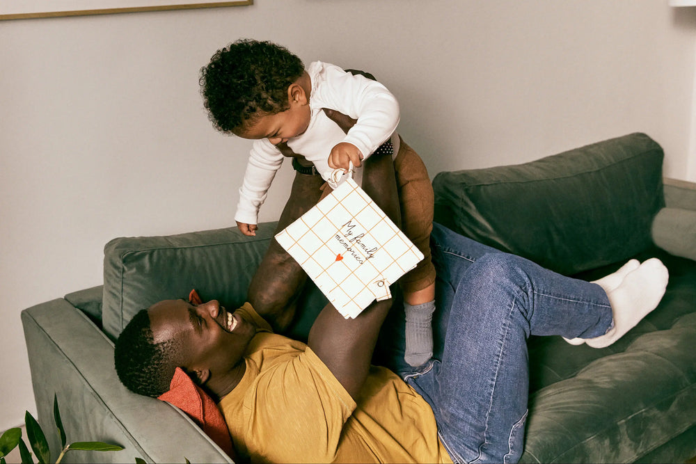 Man and child sitting on a couch with a child holding a white bag.