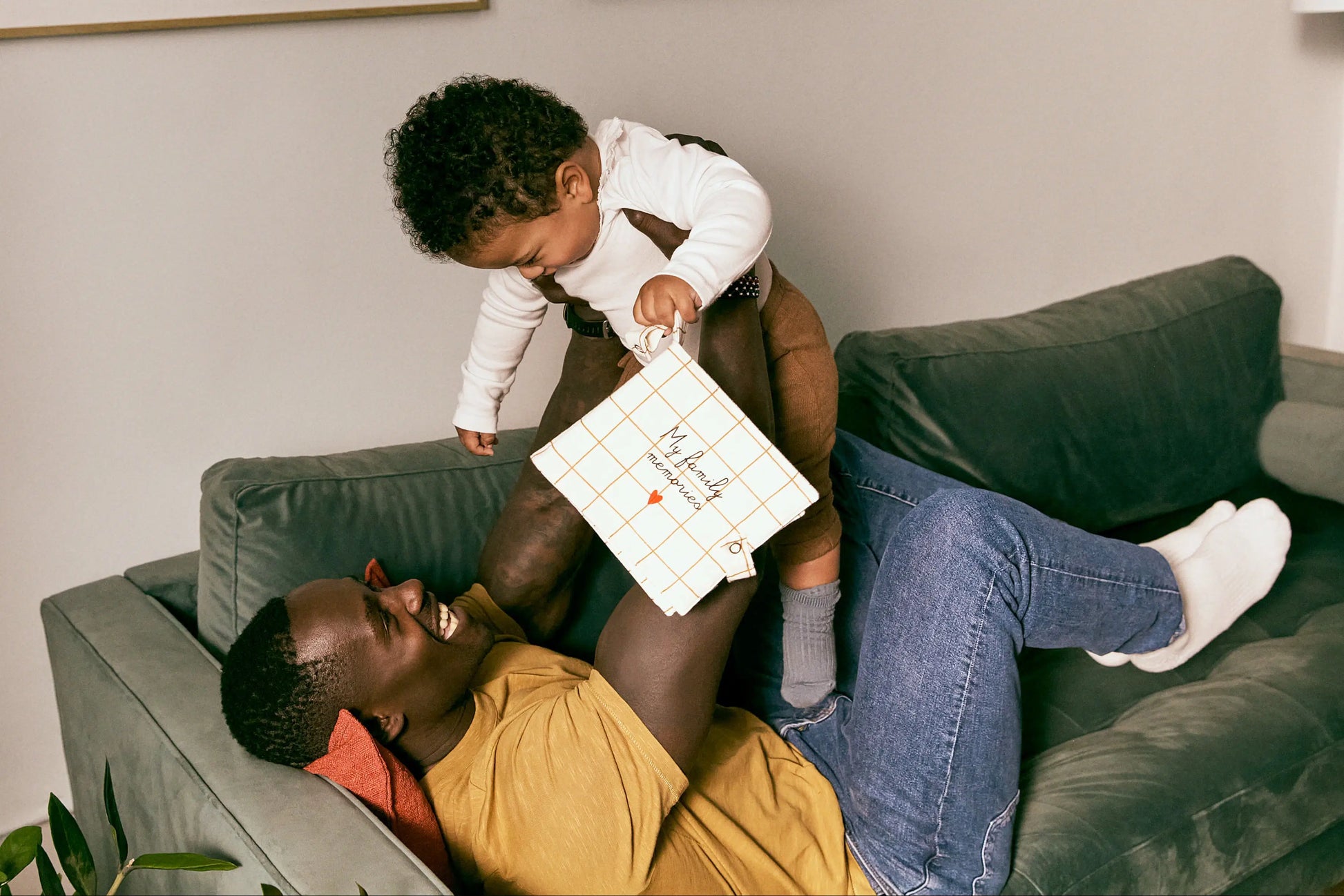 Man and child sitting on a couch with a child holding a white bag.