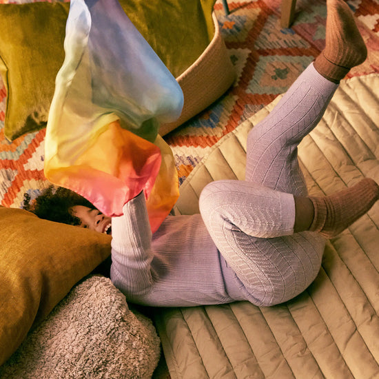 child lying on a bed with colorful pillows and a patterned blanket