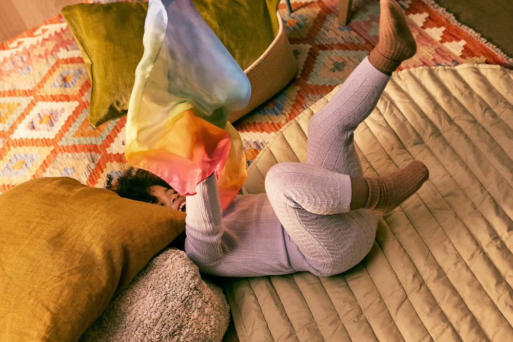 child lying on a bed with colorful pillows and a patterned blanket